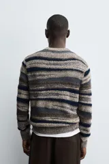 Jersey de punto con diseño de rayas horizontales en tonos tierra, azul marino y gris. Presenta cuello redondo, manga larga y terminaciones en rib acanalado.