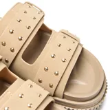 Sandalias plataforma tipo mule color taupe, con dos tiras anchas adornadas con hebillas cuadradas y remaches plateados decorativos. Cuenta con suela de plataforma alta con textura acanalada.