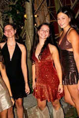 Vestido corto de tela brillante con escote en V profundo, tiras para atar al cuello y detalle de ajuste cruzado debajo del busto. Presenta un diseño entallado en la parte superior y falda con volado en el ruedo.