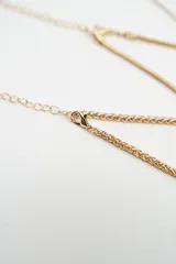 Set de tres pulseras doradas de cadena fina con cierre de mosquetón y cadena de alargue. Incluye una pulsera de cadena trenzada, una pulsera de cadena tipo serpiente con tres dijes de corazones pequeños y una pulsera de cadena tipo serpiente con un dije de corazón grande texturizado.