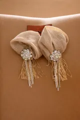 Aros colgantes con diseño de flor en rafia color beige, decorados con una pieza central de strass y flecos de hilo y cristales colgantes.