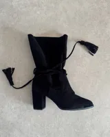 Botín de gamuza negro con taco cuadrado, caña media y tiras finas con borlas para atar alrededor del tobillo.