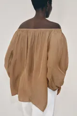 Blusa de lino color amarillo pastel, con escote recto ajustable mediante lazadas, hombros descubiertos y mangas largas abullonadas con puños elásticos.