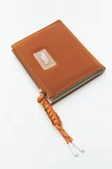 Billetera compacta de símil cuero color celeste claro, con cierre superior y un tirador de cordón trenzado multicolor. Posee un parche frontal con el logo de la marca.