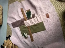 Campera sin mangas de textura tipo corderito en color rosa, con diseño de collage frontal compuesto por parches de diferentes texturas y colores en tonos tierra, verde y rosa. Incluye una etiqueta de cuero sintético con la marca.