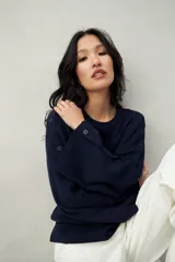 Sweater de tejido de punto color blanco hueso, con cuello redondo y mangas acampanadas. Presenta una hilera de botones a tono en el lateral de cada manga.