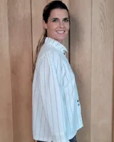 Camisa de algodón a rayas verticales blancas y azules, con cuello alto tipo gorguera con volados, cierre frontal de botones y mangas largas con puños con volados.