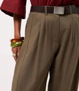 Pantalón de sintonía sastrera corte barrel color verde militar, de diseño estructurado con volumen suave en las piernas y terminación afinada. Cuenta con cintura con pasacintos, pinzas delanteras, bolsillos laterales y cinturón desmontable con hebilla metálica.