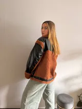 Campera negra de cuero sintético con cuello, solapas, puños y bolsillos de corderito color marrón.