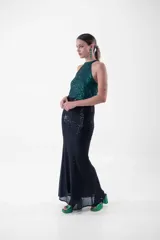 Vestido largo de fiesta con lentejuelas, compuesto por un top verde esmeralda con cuello halter y una falda negra ajustada con abertura lateral.