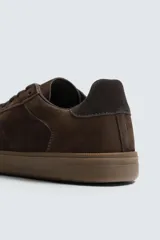 Zapatilla de estilo urbano confeccionada en piel con acabado de serraje en color marrón. Presenta cierre mediante cordones al tono, detalle de pespuntes en el empeine y suela de goma a tono.