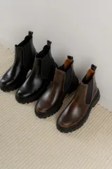 Botas tipo Chelsea de cuero con acabado vintage, diseño de caña media con paneles elásticos laterales y suela track robusta.