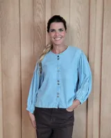 Camisa de tela liviana color celeste, con cuello redondo, cierre frontal con botones y mangas largas abullonadas con puños elásticos.