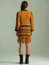 Top tejido de punto color mostaza con rayas horizontales en verde y rojo. Presenta cuello redondo, mangas largas ajustadas, hombreras y un corset integrado con rayas verticales en verde.