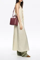 Bolso pequeño de piel color borgoña, con estructura rígida y forma de cubo. Posee doble asa de mano y una correa larga para llevar al hombro o cruzado. El frente lleva el logo metálico de Bimba y Lola.