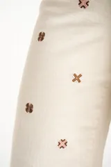 Jean de corte recto y tiro medio, color off-white, con diseño de pequeños bordados en forma de cruz distribuidos por toda la prenda.