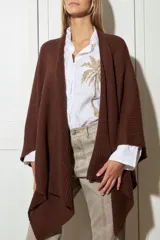 Ruana tejida en punto marrón oscuro, de corte envolvente y sin mangas, ideal para superponer sobre otras prendas.