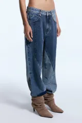 Pantalón de jean con diseño de patchwork que combina diferentes tonos de denim en paneles geométricos. Presenta un corte relajado, tiro medio y cierre frontal con botón metálico.