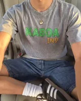 Remera de corte oversize color gris con efecto stone wash y estampa frontal con el texto KABOA IND en colores verde y naranja.