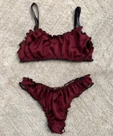 Conjunto de lencería compuesto por un corpiño tipo bralette y una bombacha colaless, confeccionados en satén color bordó con terminaciones fruncidas y bordes en contraste negro. El corpiño cuenta con breteles finos ajustables y diseño de doble tela, mientras que la bombacha presenta un corte cavado con refuerzo de algodón.