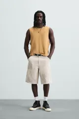 Bermuda de algodón color beige claro con efecto lavado y estampado abstracto en tonos grises. Diseño de corte relajado con cierre frontal de botón y cremallera, bolsillos delanteros y bolsillos traseros de plastrón.