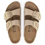 Sandalia Birkenstock modelo Arizona Big Buckle, con dos correas anchas de cuero nobuck en color beige y hebillas grandes metálicas doradas. Cuenta con plantilla anatómica de corcho y suela de goma.