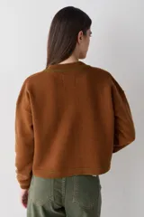 Cardigan de punto color marrón con detalles de ribete en color verde oliva en cuello, puños, ruedo y tapeta de botones. Presenta cierre frontal con botones grandes y un pequeño bordado en el pecho.