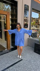 Vestido corto de manga larga con volados, color lavanda, con cuello camisero y botones frontales.