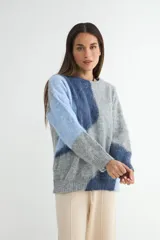 Buzo de tejido de punto con diseño de bloques de color en tonos blanco y gris, de cuello redondo y manga larga.