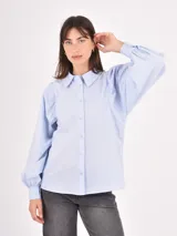 Camisa de manga larga en color celeste, con cuello clásico y cierre frontal de botones. Presenta un diseño con mangas abullonadas y puños ajustados.