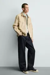 Cazadora relaxed fit de Zara confeccionada en denim de algodón color beige, con cuello de solapa en piel combinada, bolsillos con cremallera en el pecho y cierre frontal oculto.