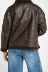 Campera tipo gamulán de corte oversize, color marrón oscuro con efecto cuero envejecido. Presenta cuello solapa, puños y ruedo con forro de corderito sintético en tono marrón oscuro. Cuenta con cierre frontal completo y detalles de costuras reforzadas.