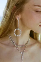 Pendientes colgantes metálicos con diseño de barra vertical y doble aro, decorados con incrustaciones de joyas brillantes. Cierre con tuerca.