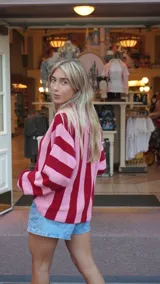 Cárdigan con rayas verticales rojas y rosadas, cuello polo y cierre frontal con botones.