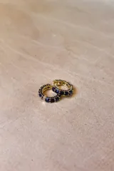 Aros tipo argolla pequeña de base metálica dorada con incrustaciones de cristales transparentes en la parte frontal.