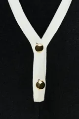 Vestido corto de tejido suave, color negro con detalles en blanco. Presenta cuello solapa, escote en pico, manga larga, falsos bolsillos delanteros y cierre frontal con botones dorados.