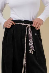 Pantalón wide leg de tiro alto en color negro, con diseño de pinzas delanteras que aportan volumen y caída fluida. Incluye bolsillos laterales y un lazo desmontable en la cintura que combina cordón con cinta de estampado animal print.