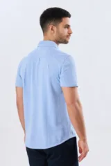 Camisa de piqué lisa color celeste, de manga corta, con cuello camisero y cierre frontal de botones oscuros.