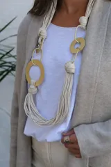 Collar largo de diseño artesanal compuesto por múltiples cordones de algodón en color crudo, entrelazados con aros y eslabones metálicos en tono dorado mate.