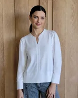 Remera blanca de manga larga con cuello mao y escote en V. Presenta un diseño con pliegues frontales, hombros ligeramente abullonados y puños anchos.