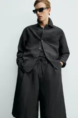 Bermuda relaxed fit de color negro, confeccionada en tejido fluido con viscosa y modal. Presenta cintura elástica ajustable con cordón, pliegues en el delantero, bolsillos frontales y bolsillos traseros de vivo.