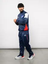 Conjunto deportivo Umbro del Club Nacional de Football, compuesto por una campera con cierre frontal y un pantalón a juego. Ambas piezas son de color azul marino con detalles en blanco y rojo, presentando el escudo del club y el logo de la marca.