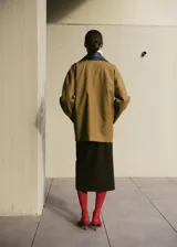 Chaqueta de corte amplio en tono tostado, con solapas y cuello de cuero sintético en color negro kontrastante. Posee cierre frontal de botones oscuros y bolsillos laterales discretos.