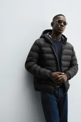 Campera puffer acolchada de corte regular fit en color negro, confeccionada en tejido técnico repelente al agua. Presenta cuello subido con capucha, cierre frontal de cremallera, mangas largas con puños elásticos y bolsillos laterales de vivo.