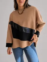 Buzo de punto con diseño oversize y calce relajado. Presenta bloques de color en tonos tostado y negro, con una franja diagonal en material brillante texturizado. Posee cuello redondo, mangas largas con puños negros y un corte asimétrico con el largo trasero ligeramente mayor al delantero.