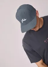 Gorro tipo gorra con visera de color gris oscuro, con el logo de la marca Rusty bordado en color blanco en el frente.