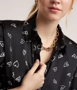 Vestido corto modelo chemise, color negro con estampado de corazones blancos, de manga larga abullonada con hombreras y puños ajustados. Incluye cinturón para lazo en la cintura.