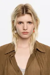 Pendientes de aro dorados con diseño asimétrico de la marca Bimba y Lola. Una de las caravanas incluye un dije de perla blanca y la otra un dije de corazón rojo esmaltado con el logo de la marca grabado.