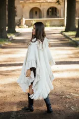 Ruana de lana merino color crudo, con diseño de silueta amplia y caída fluida. Presenta detalles de volados en lino a lo largo de la prenda y terminaciones con flecos en el ruedo.