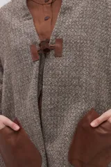 Chal de lana fina sin teñir con diseño de cuadros sutiles, cierre frontal con alamar y bolsillos de cuero metalizado. Presenta terminaciones con flecos en el ruedo y un calce estructurado en los hombros.